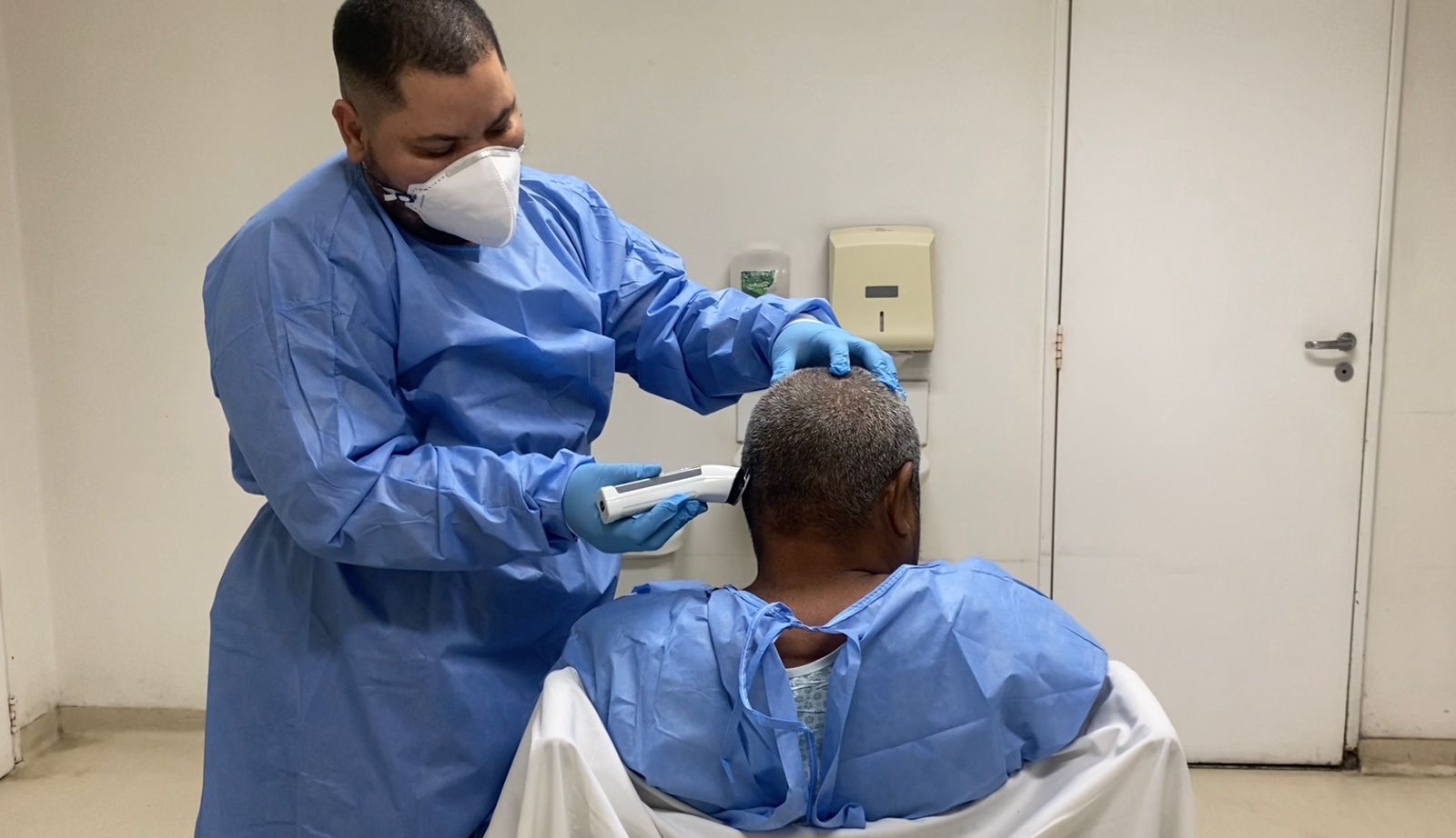 Richard está cuidando de um paciente que está sentado de costas. O técnico em enfermagem cortando o cabelo do paciente. 